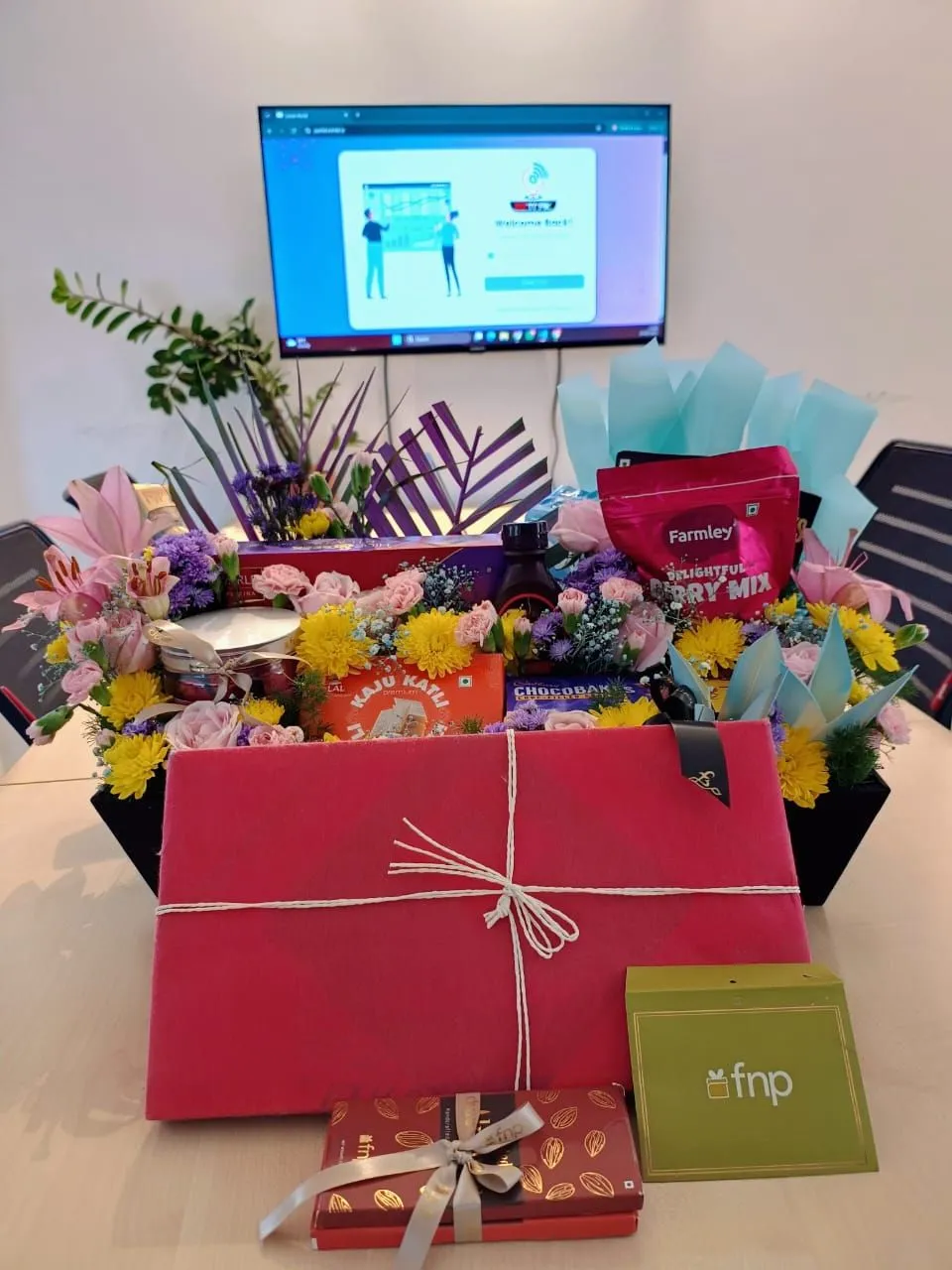 The gift up close, a basket of flowers, sweets and snacks with a wrapped present and a card, in front of the EZTrak sign-in screen.