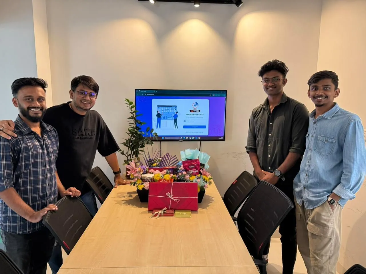 Four of us from the Mobil80 team around a meeting table with the client's gift basket, and the EZTrak sign-in screen on the TV behind.